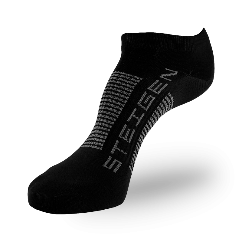 A sleek, black ankle-length performance sock. The brand name "STEIGEN" is printed vertically in grey, accompanied by a grey textured or dotted pattern on the bridge and side of the foot for ventilation or grip. The image is set against a transparent grid background.