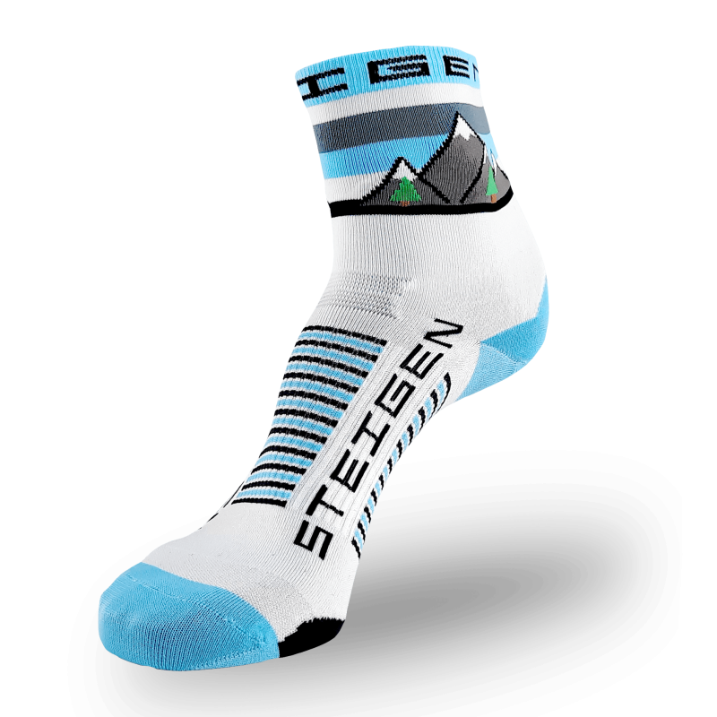 A white Steigen athletic sock featuring a detailed landscape graphic on the cuff depicting grey mountains with snow caps and small green evergreen trees. The toe and heel are light blue, and the brand name is printed vertically in black on the foot next to light blue and black arch stripes.