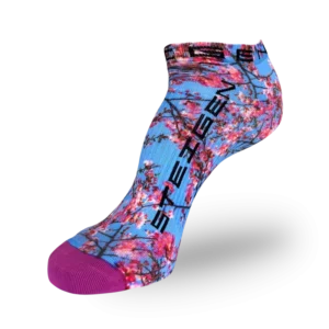 A low-cut athletic sock featuring a light blue base covered in a pink cherry blossom print with dark brown branches. The brand name "STEIGEN" is printed in bold black text vertically down the side. The sock has a solid purple reinforced toe.