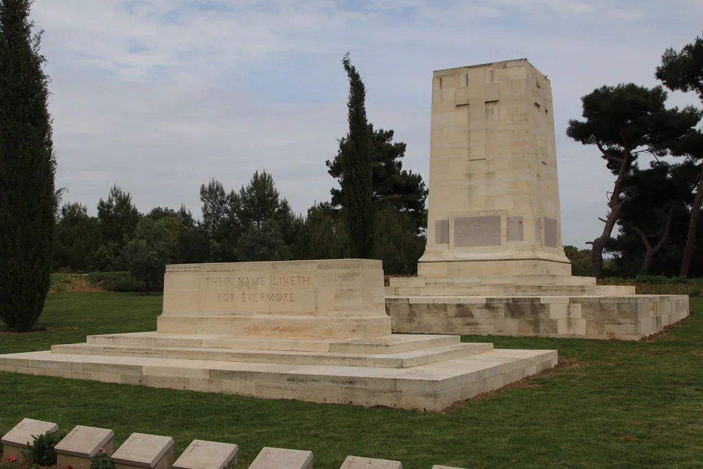 Two large, light-colored stone monuments sit on a green lawn. The foreground stone is inscribed with "THEIR NAME LIVETH FOR EVERMORE," while the background stone is a tall pylon featuring a carved cross.