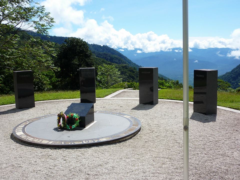 A close-up of a circular stone memorial on a mountain ridge featuring four black granite pillars inscribed with "Courage," "Endurance," "Mateship," and "Sacrifice".