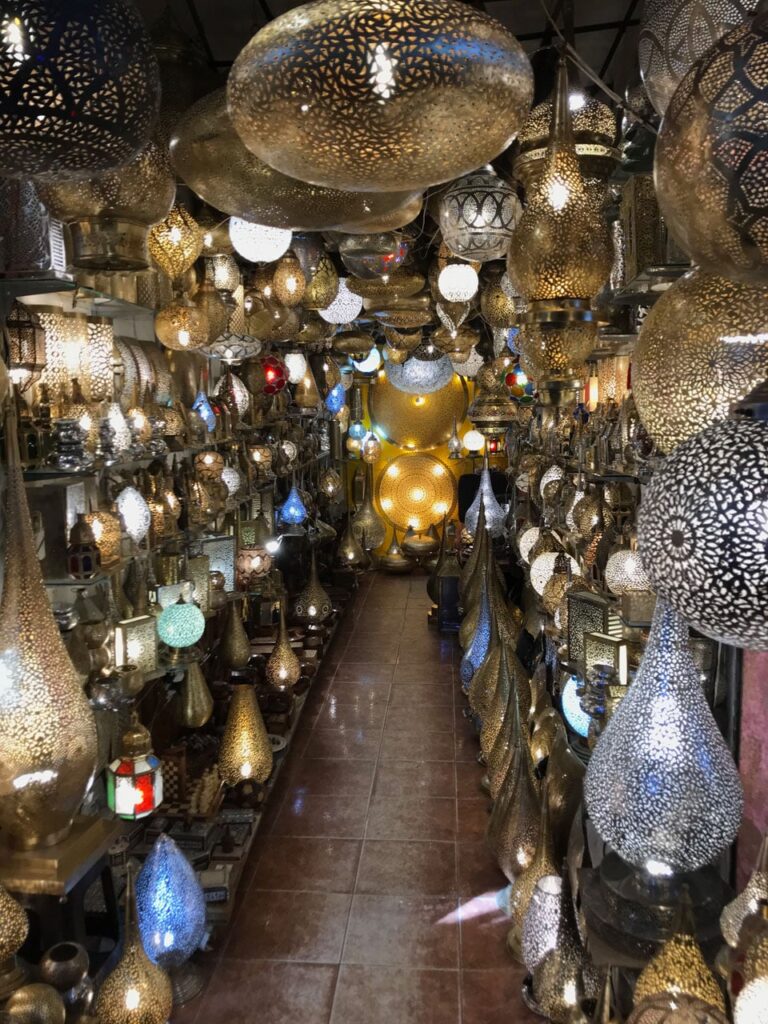 A dazzling shop interior filled with glowing, intricately carved Moroccan metal lanterns in gold and blue hues.