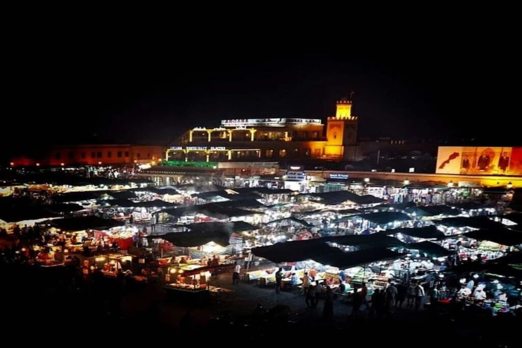A bustling night view of the illuminated food stalls and crowds in Jemaa el-Fnaa square, Marrakesh.