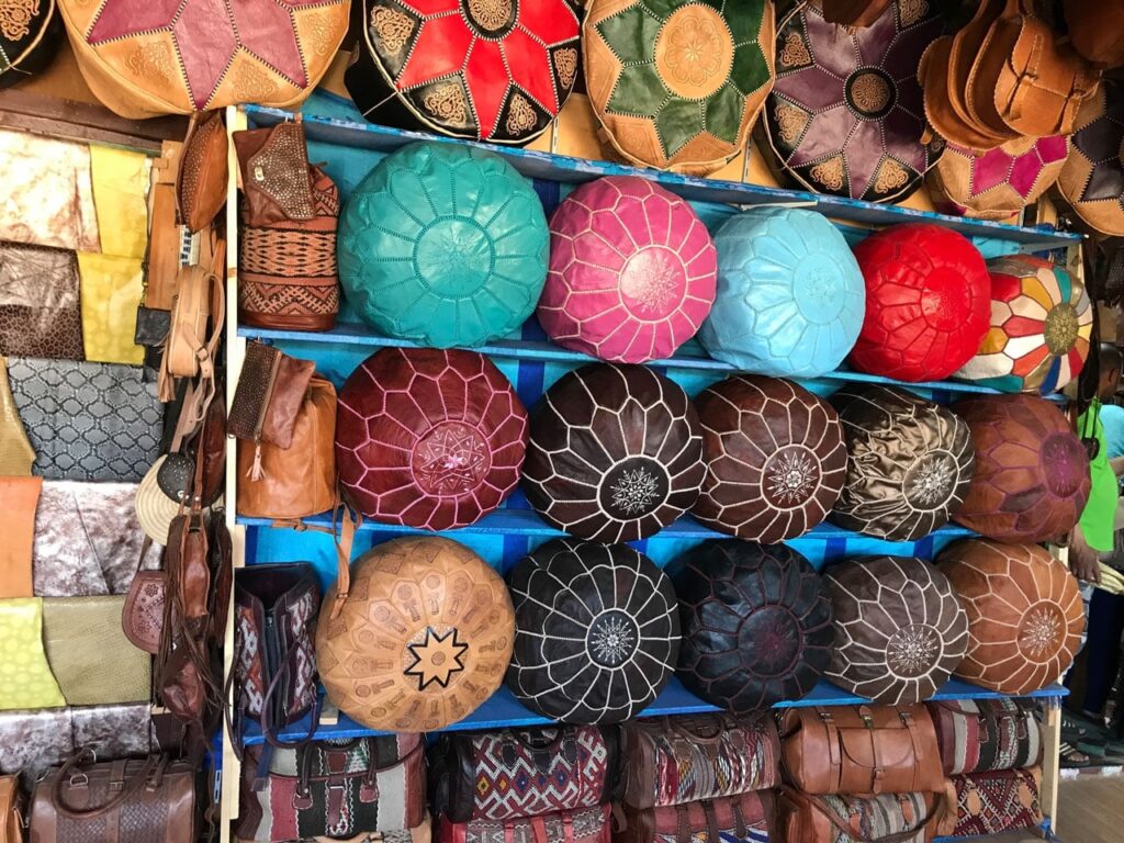 A bright market stall in Morocco featuring a variety of colorful embroidered leather poufs and handmade bags.